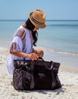 Person at beach wearing straw Essential Hat and looking into large black mesh bag