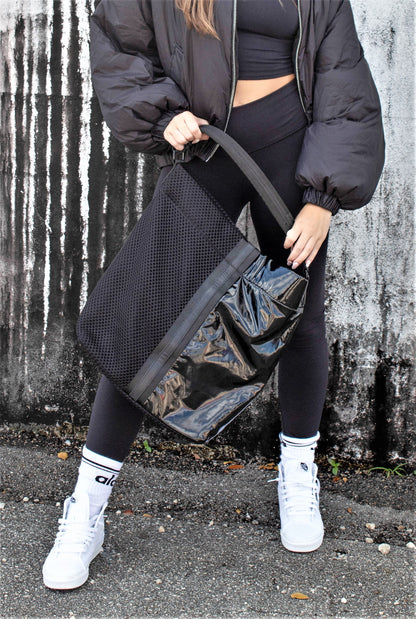 person with black mesh and glossy vinyl sporty tote bag with black leather and webbing details.
