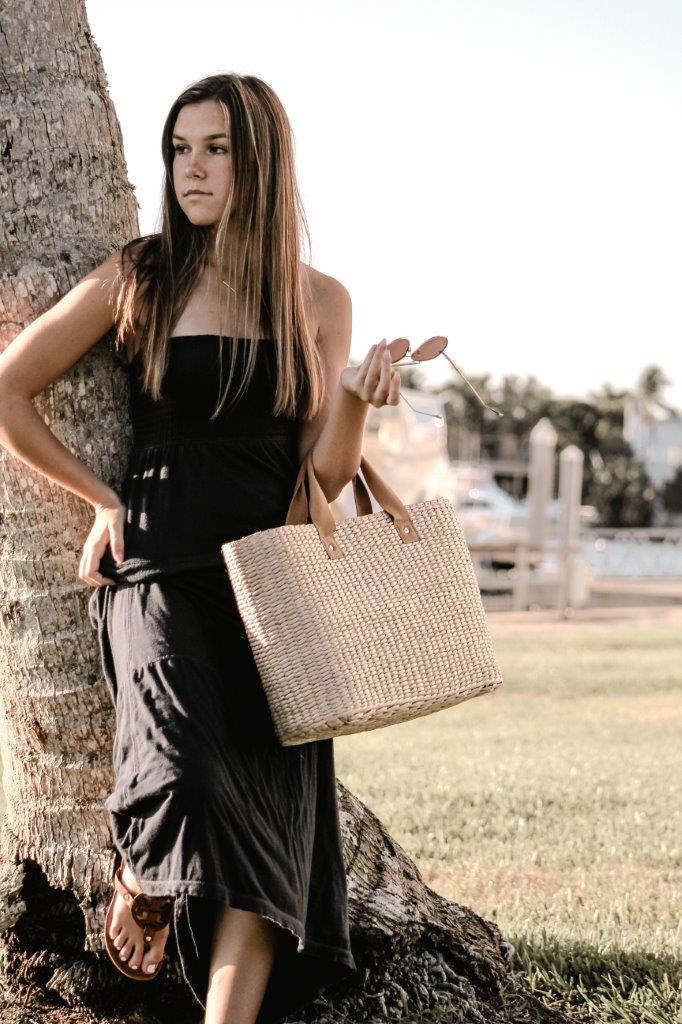 person leaning on tree holding straw bag with leather handles