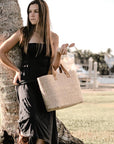 person leaning on tree holding straw bag with leather handles