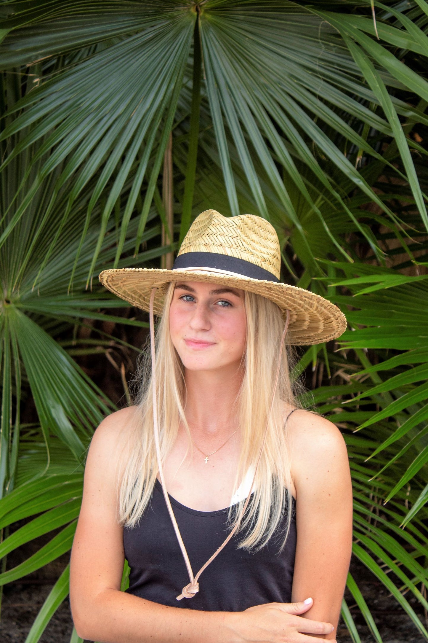 Person wearing the Tower Hat - a straw lifeguard hat with tan leather chin strap and black band detail.