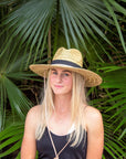 Person wearing the Tower Hat - a straw lifeguard hat with tan leather chin strap and black band detail.