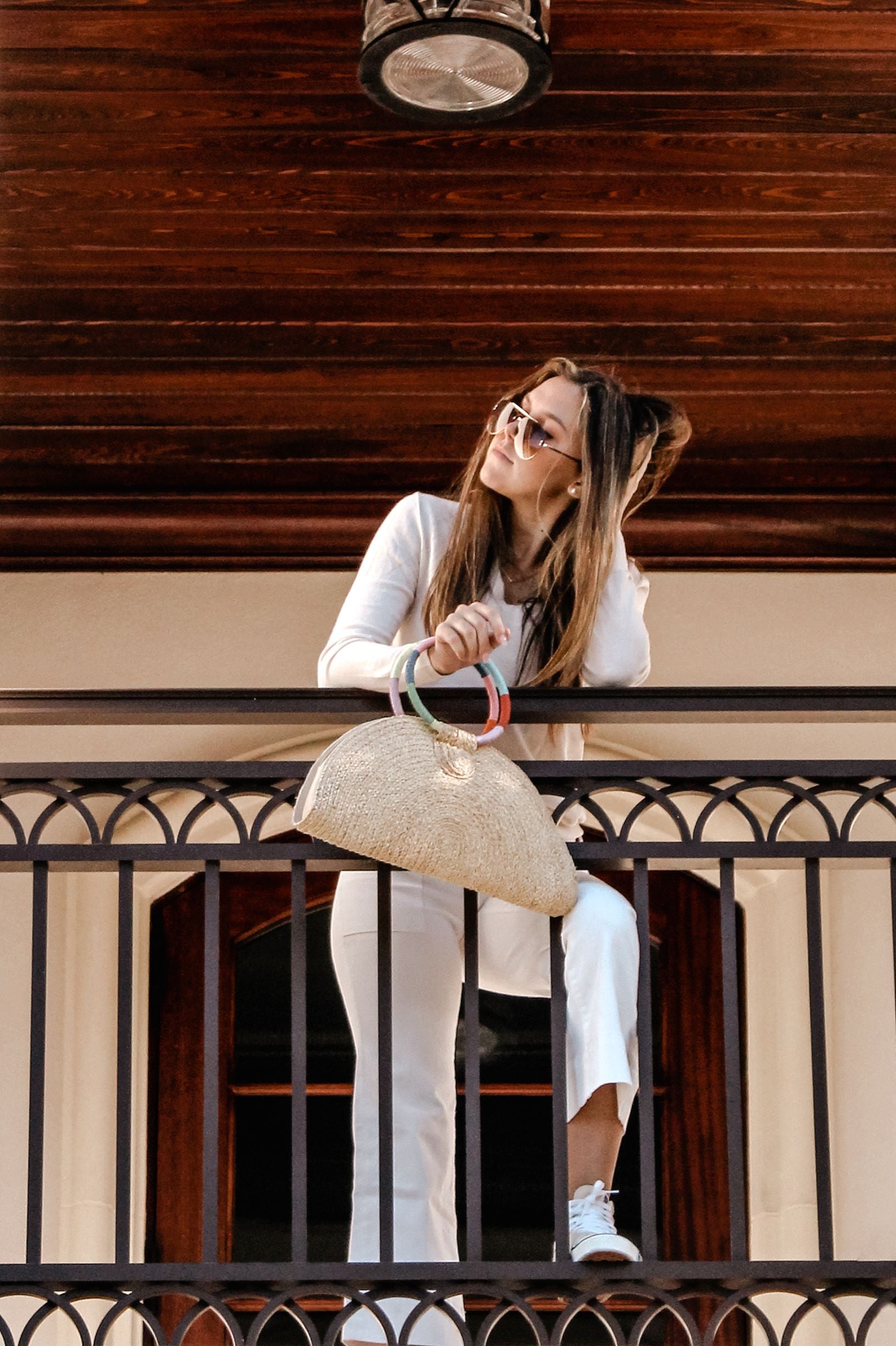 Person holding natural raffia straw half-moon clutch with rainbow colored wrapped circle handle and leather sides.