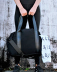 Person holding the Stanton Duffel bag in black, with the Anya & Niki sports towel in the pocket.