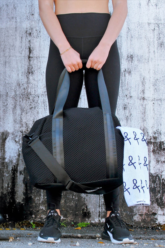 person holding black mesh duffel bag with leather trim details and black glossy liner.