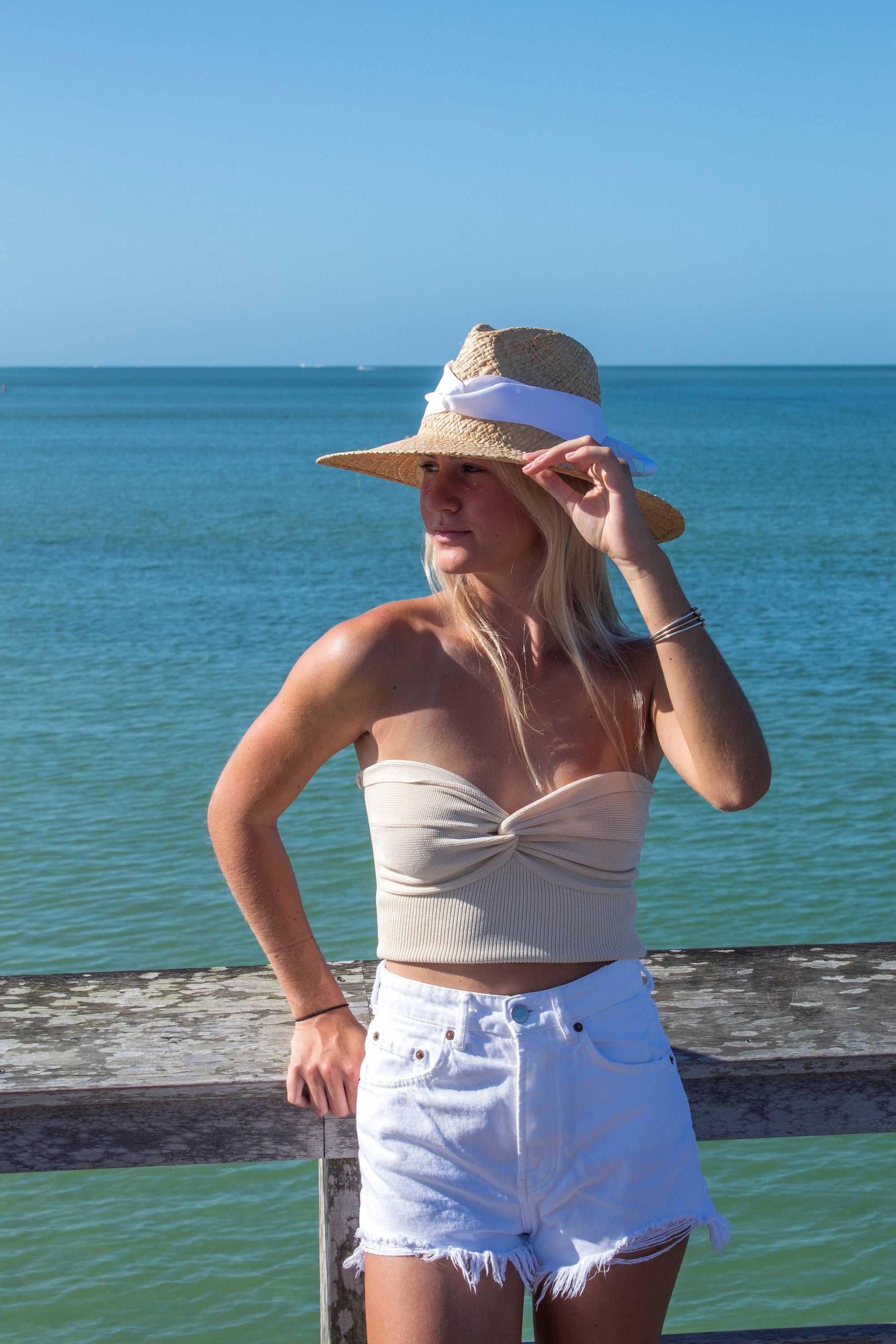 Person wearing the Everywhere Hat - a natural raffia straw panama hat with white grosgrain tie.