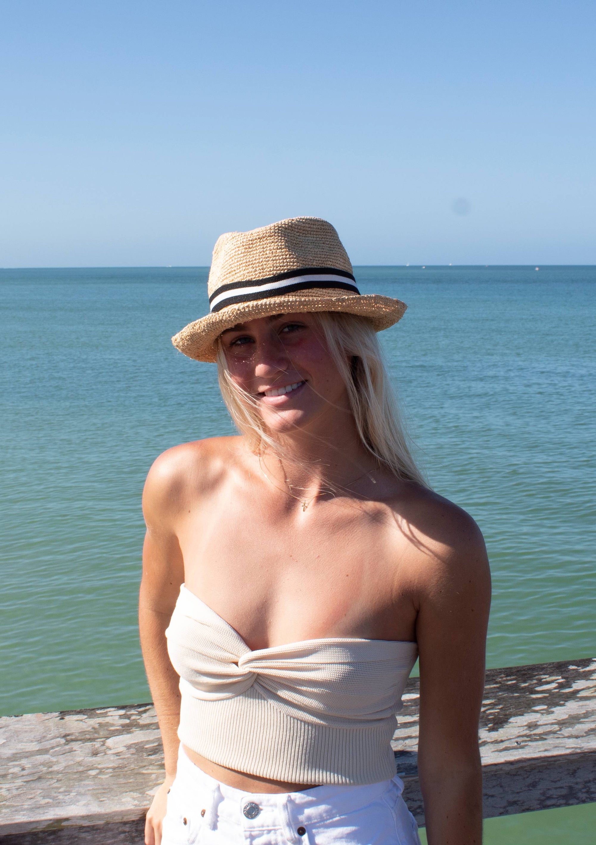 Person wearing natural colored crochet straw fedora hat with black &amp; white stripe band.