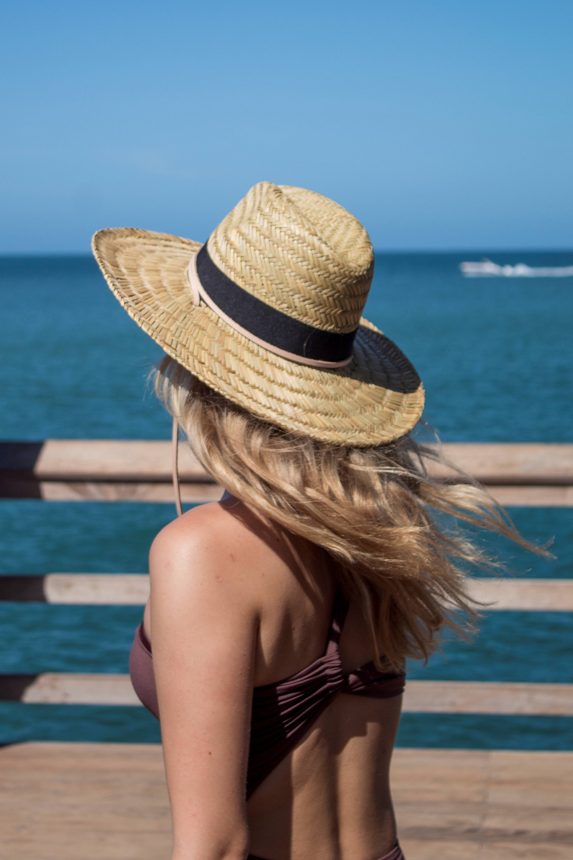 Person wearing the Tower Hat - a straw lifeguard hat with tan leather chin strap and black band detail.