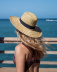 Person wearing the Tower Hat - a straw lifeguard hat with tan leather chin strap and black band detail.