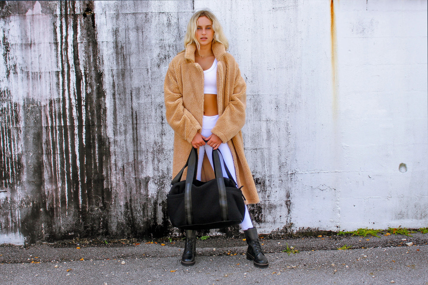 Person wearing the Anya & Niki Stanton Bag - a black mesh duffel bag with leather trim details and black glossy liner.