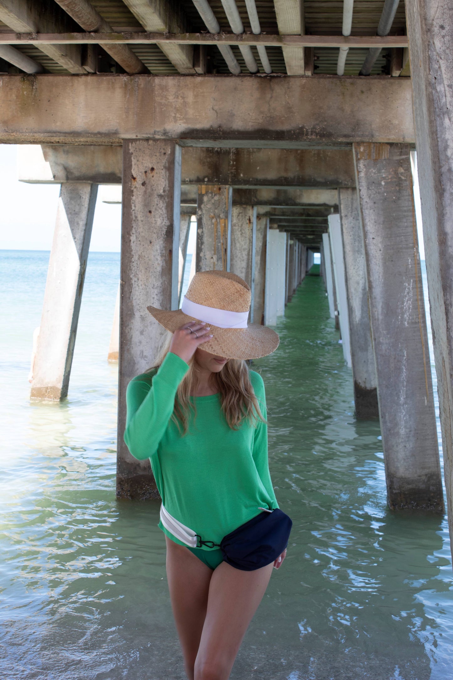 Person wearing the Everywhere Hat - a natural raffia straw panama hat with white grosgrain tie and the Orlando Navy belt bag.