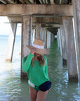 Person wearing the Everywhere Hat - a natural raffia straw panama hat with white grosgrain tie and the Orlando Navy belt bag.