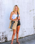 Person holding the Benicia straw tote bag with black leather handles and black & white center stripe.