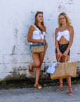 Two people holding straw bags in mini verson with white crossbody strap and large version with leather handles