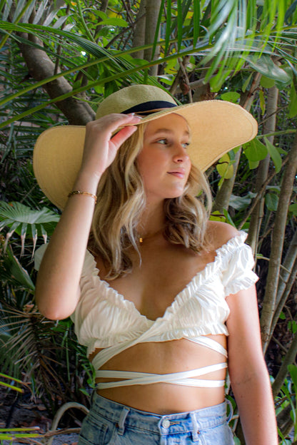 Person wearing the Big Hat Natural - a floppy straw hat with black grosgrain ribbon and thin brown leather band.