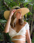 Person wearing the Big Hat Natural - a floppy straw hat with black grosgrain ribbon and thin brown leather band.