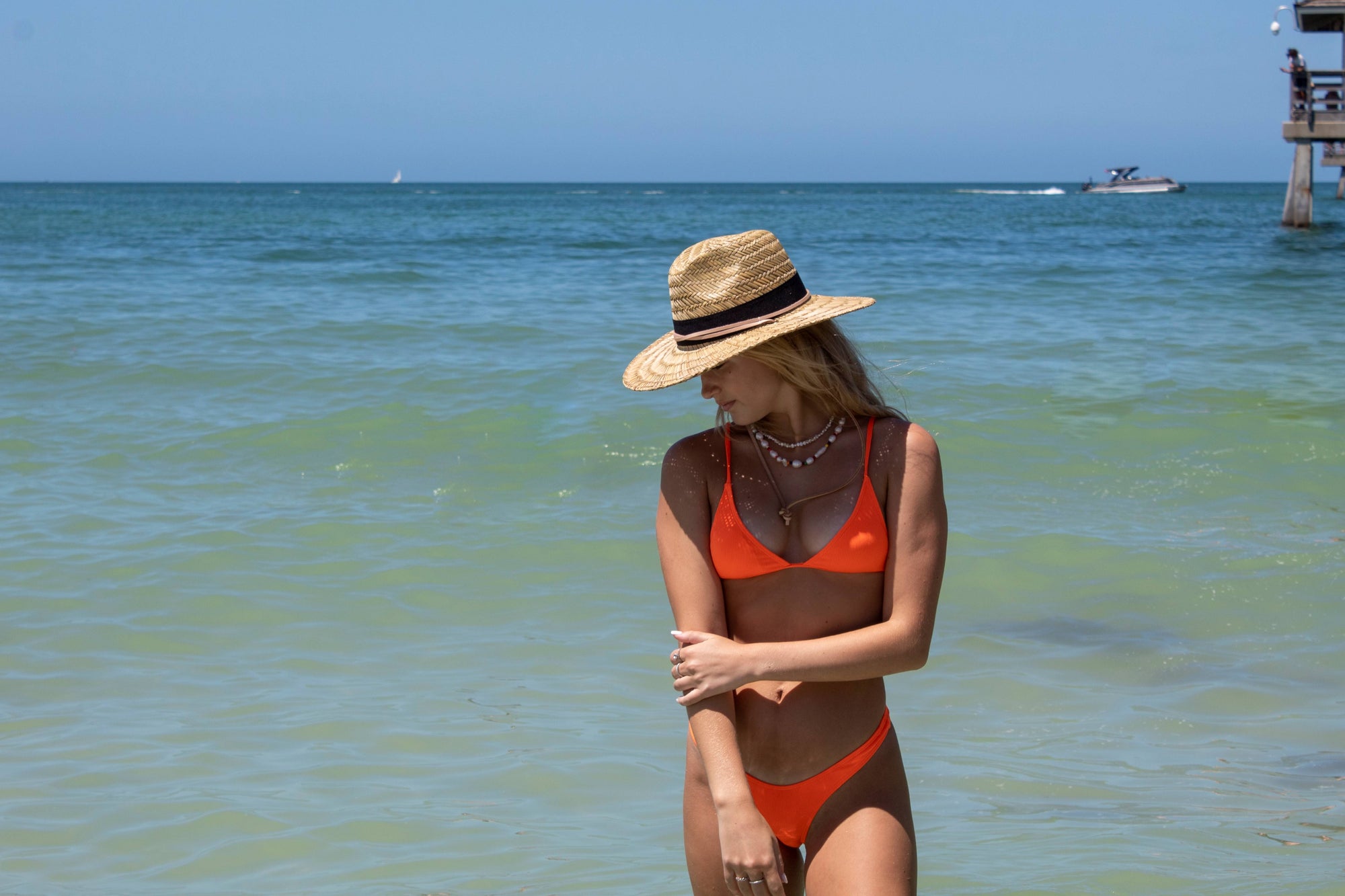 Person wearing the Tower Hat - a straw lifeguard hat with tan leather chin strap and black band detail.