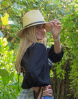 Person wearing a natural straw panama hat with thin brown leather band.