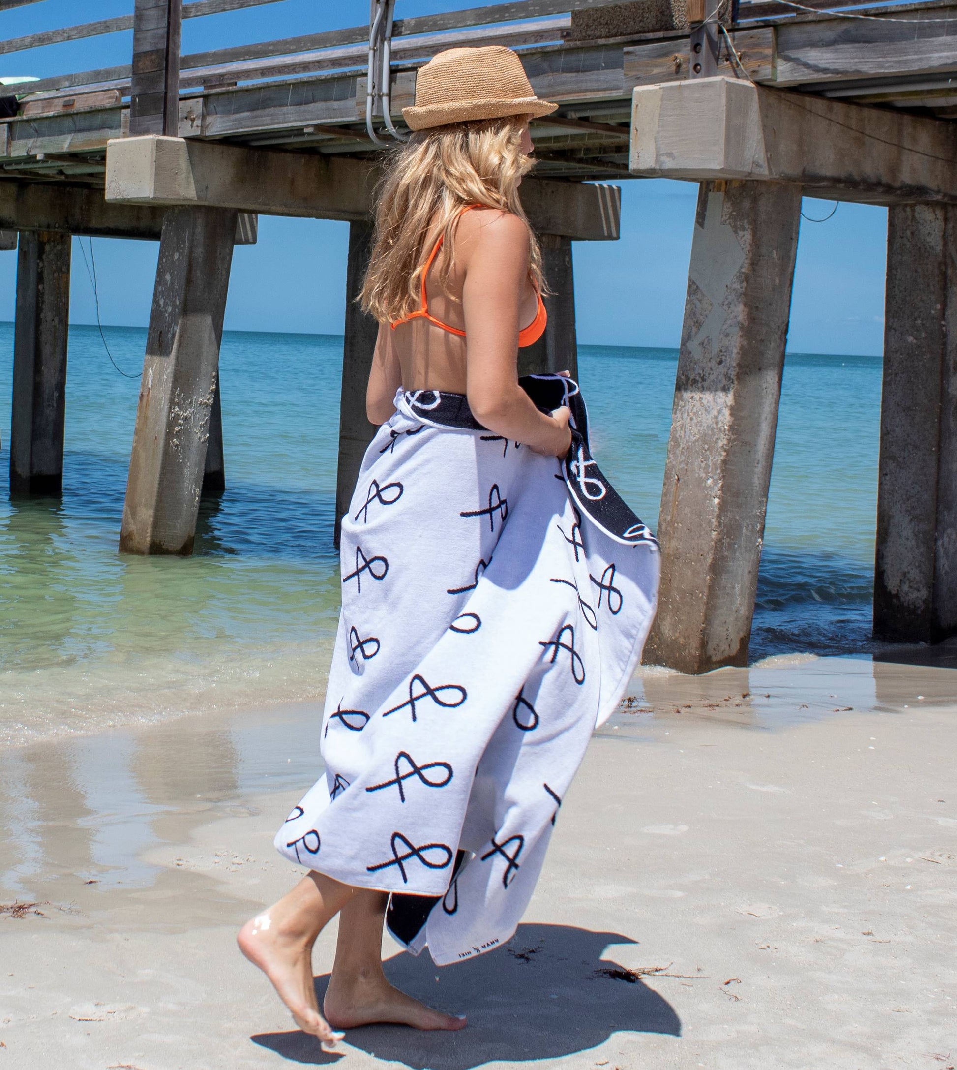 Person at beach wearing the Anya & Niki large beach towel and wearing the Essential Straw Hat