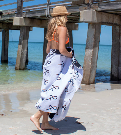 Person at beach wearing the Anya & Niki large beach towel and wearing the Essential Straw Hat