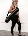 Person holding Anya & Niki glossy black yoga mat bag.