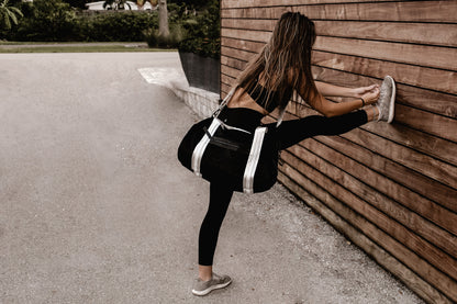 person wearing black velour duffel bag with white straps and leather details, while stretching on wood wall.