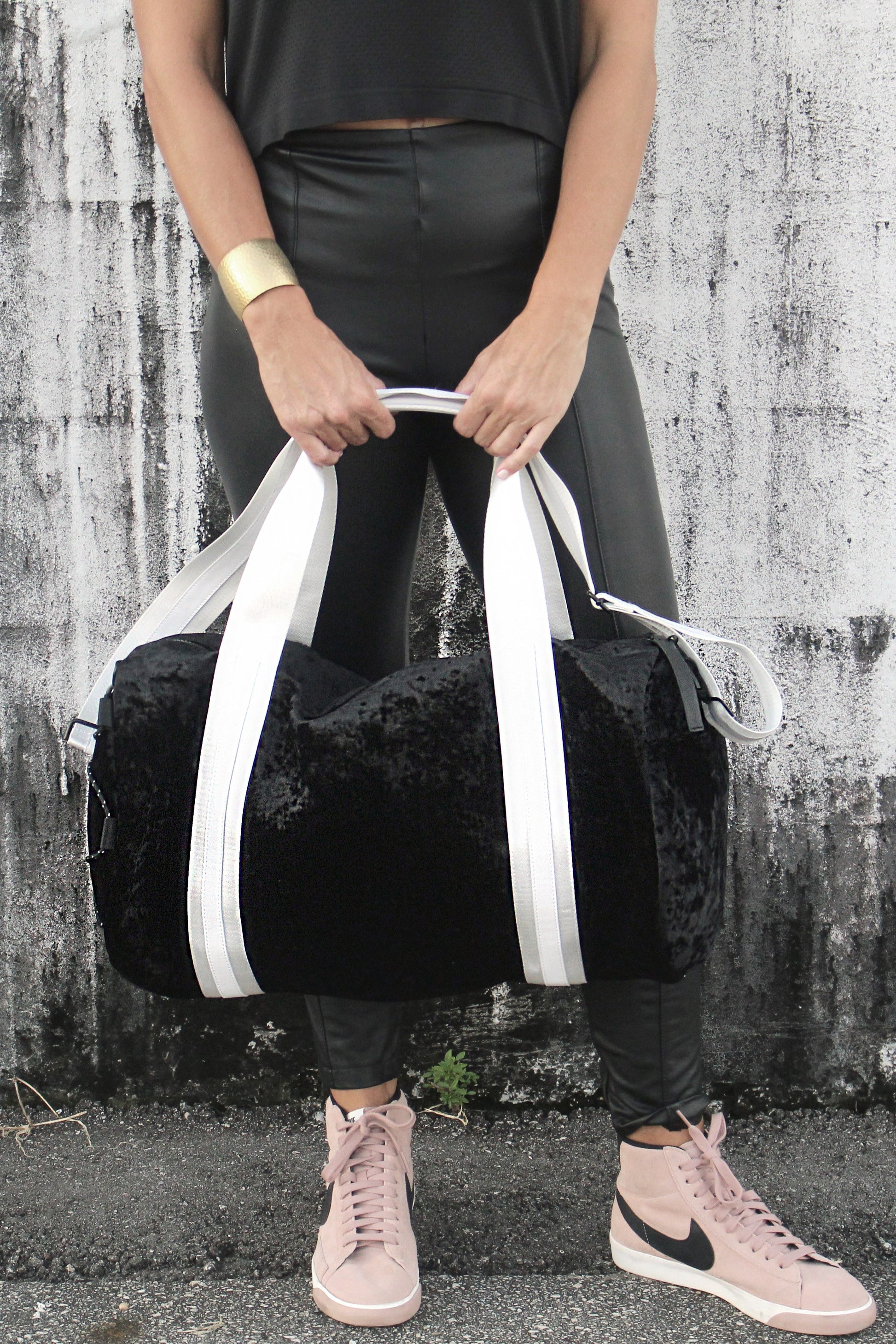 person holding black velour duffel bag with white straps and leather details