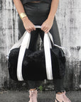 person holding black velour duffel bag with white straps and leather details