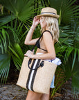 Person holding the Benicia straw tote bag with black leather handles and black & white center stripe.