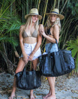 Two people holding black mesh beach bag with leather details in med and large size