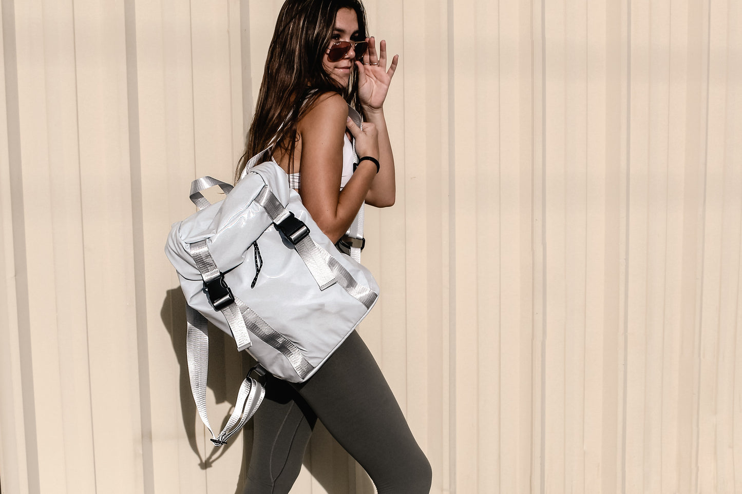 Person holding gray high gloss backpack with gray leather and webbing details.