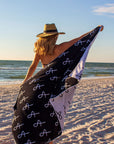 Person at beach holding Anya & Niki large beach towel and wearing the Tower Straw Hat