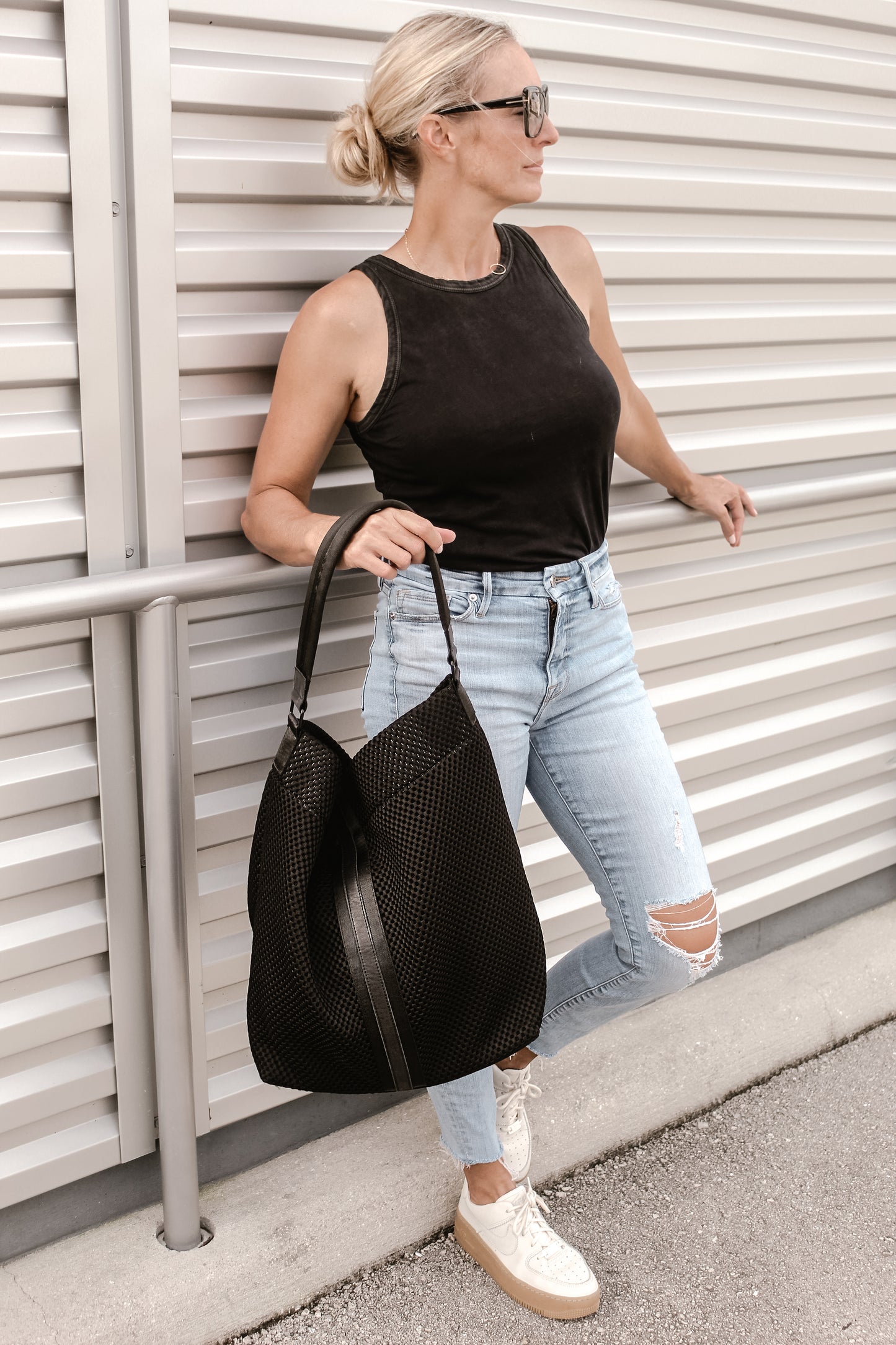 Person holding black sporty mesh tote bag with black leather and webbing details.