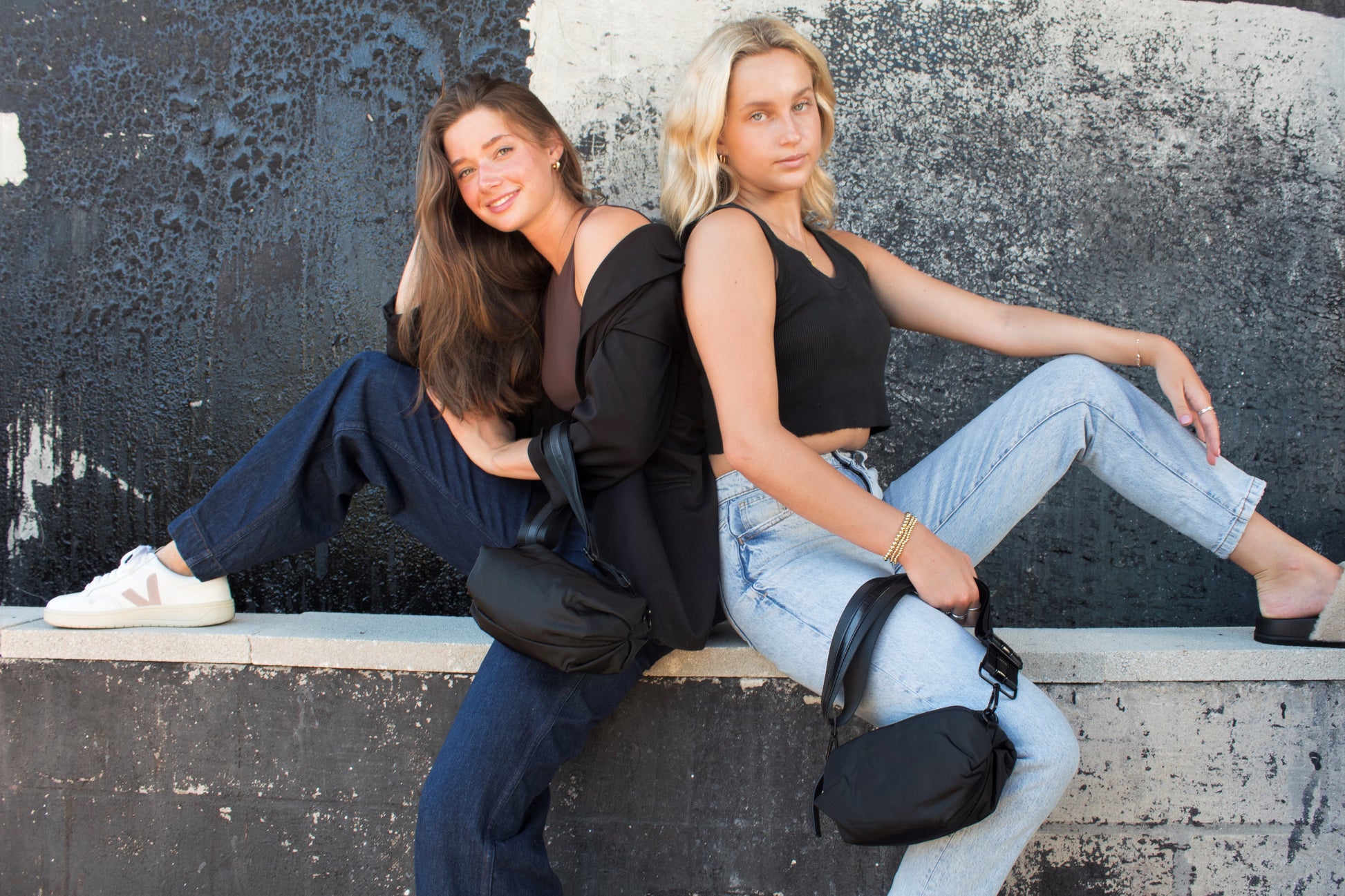 Two people sitting holding the Anya & Niki Orlando Black Belt Bag: one with black leather detail and one with shiny black leather detail,