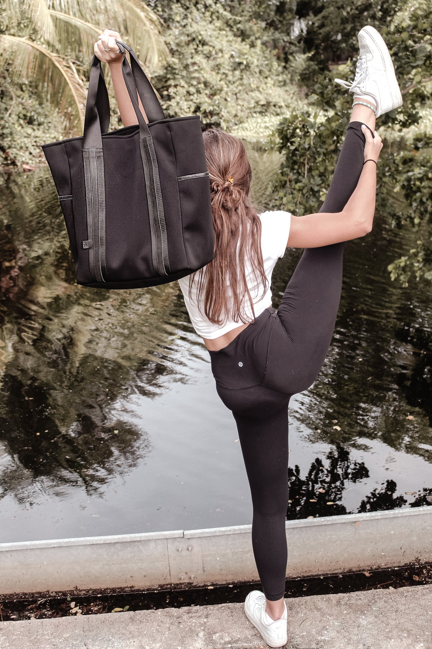 Person holding the Anya & Niki Hawthorne Tote - a black neoprene tote bag with high shine cinch top closure and leather details.
