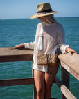 Person wearing the Hampton mini straw bag with white crossobdy strap with leather details and the Tower straw hat