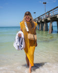 Person wearing the Hampton mini straw bag with white crossobdy strap with leather details and holidng the A&N Beach Towel