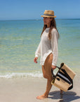 Person holding the Benicia straw tote bag with black leather handles and black & white center stripe wtih black crossbody strap.