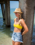 Person at the beach wearing the Anya & Niki Essential Hat - a natural colored crochet straw fedora hat with ivory rope band.