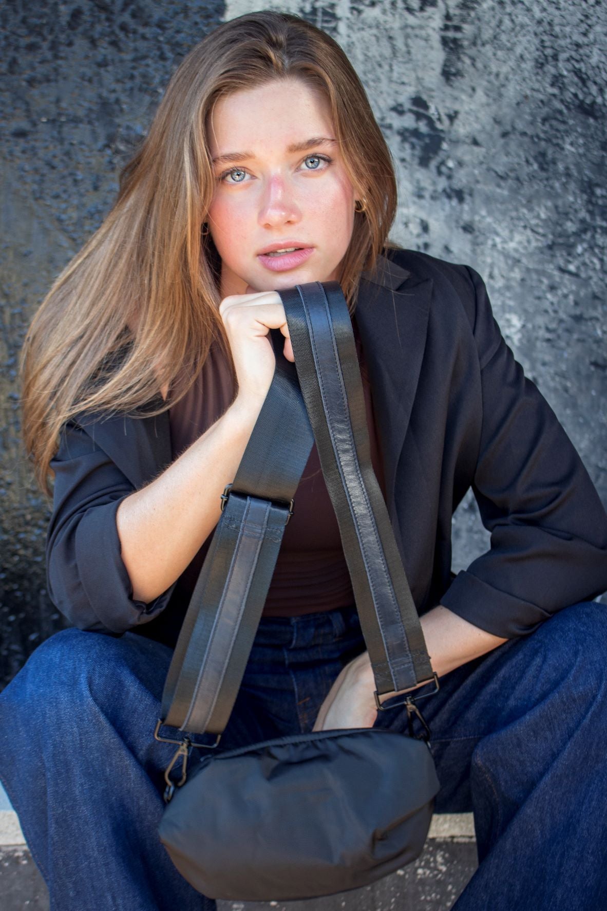 Person holding black nylon belt bag with black crossbody strap with black leather detail