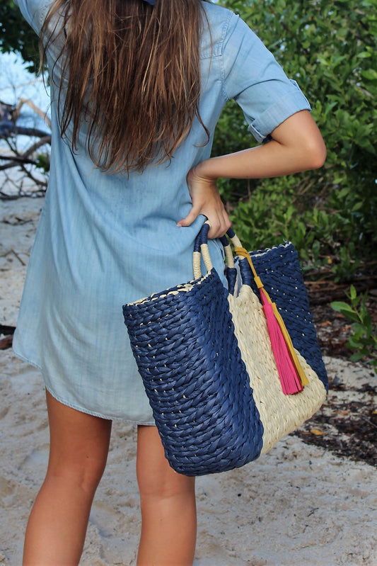Person holding the Anya & Niki Isla straw bag - a navy and natural colored over-sized straw tote with circle handle and suede tassels.