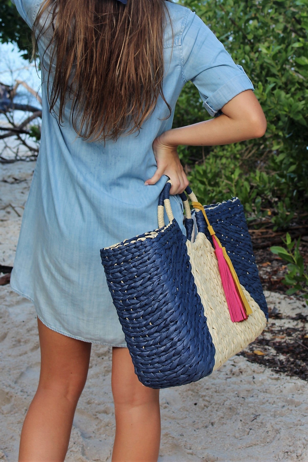 Person holding the Anya &amp; Niki Isla straw bag - a navy and natural colored over-sized straw tote with circle handle and suede tassels.