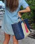 Person holding the Anya & Niki Isla straw bag - a navy and natural colored over-sized straw tote with circle handle and suede tassels.