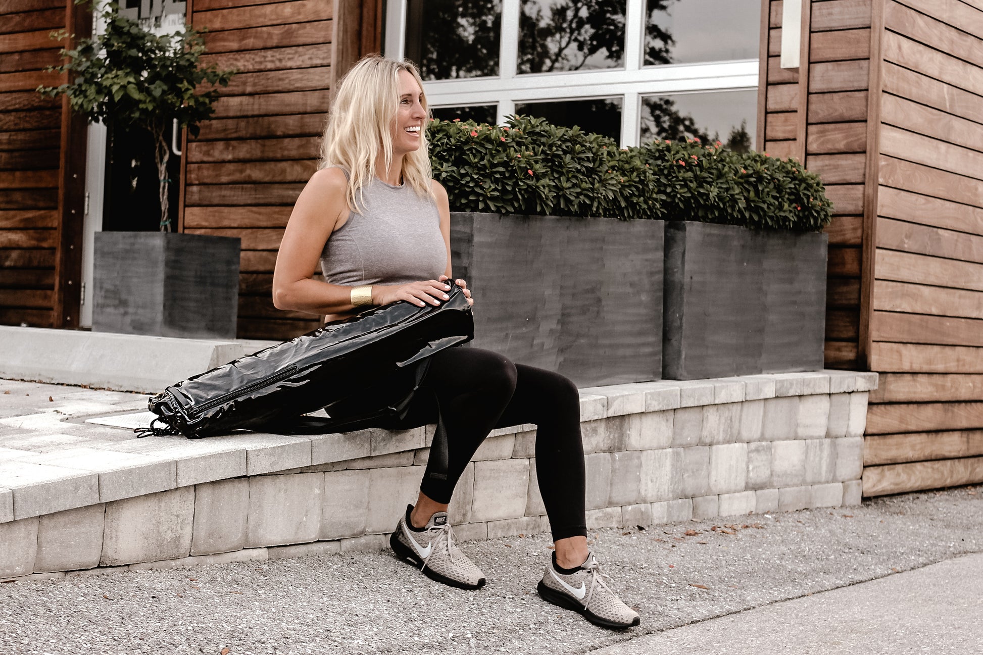 Person sitting on steps with Anya & Niki glossy black yoga mat bag.