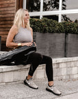 Person sitting on steps with Anya & Niki glossy black yoga mat bag.