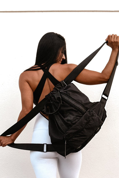 Person holding the Anya & Niki Davie Backpack. A black nylon convertible backpack tote with leather details.