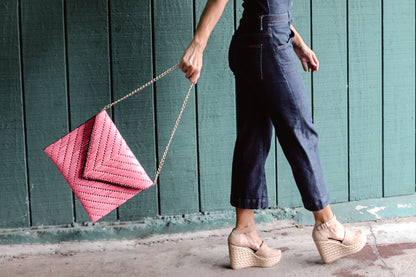 person holding bright pink woven raffia straw clutch by detachable gold chain strap. 