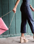 person holding bright pink woven raffia straw clutch by detachable gold chain strap. 