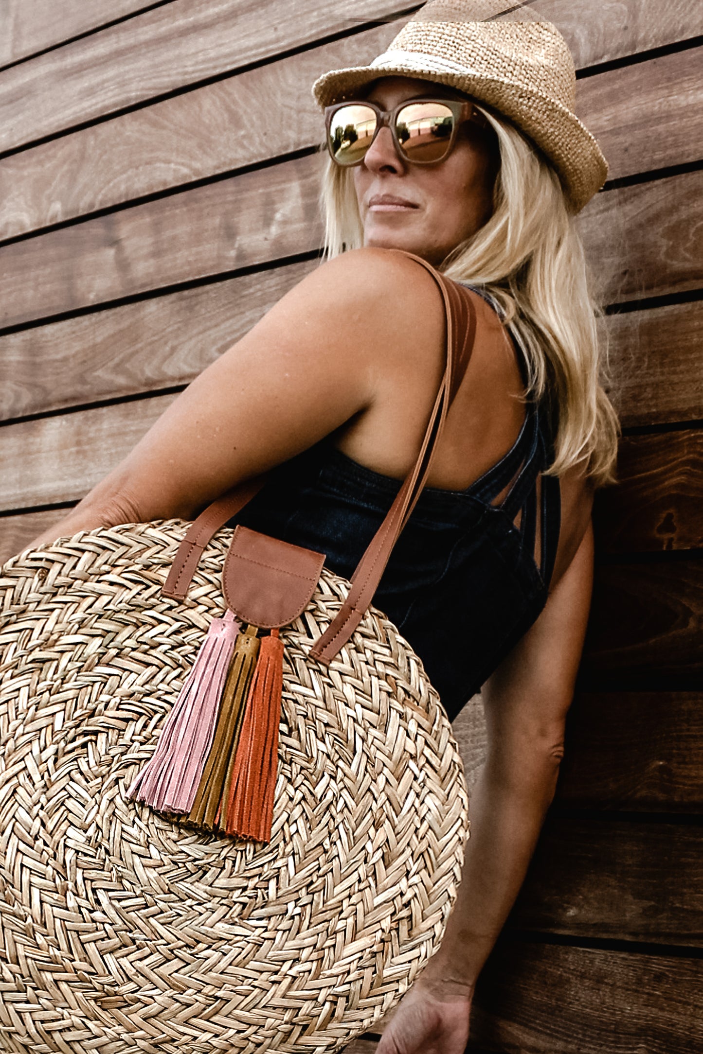person wearing seagrass round straw bag with leather handles and suede tassel closure and crochet straw fedora. 