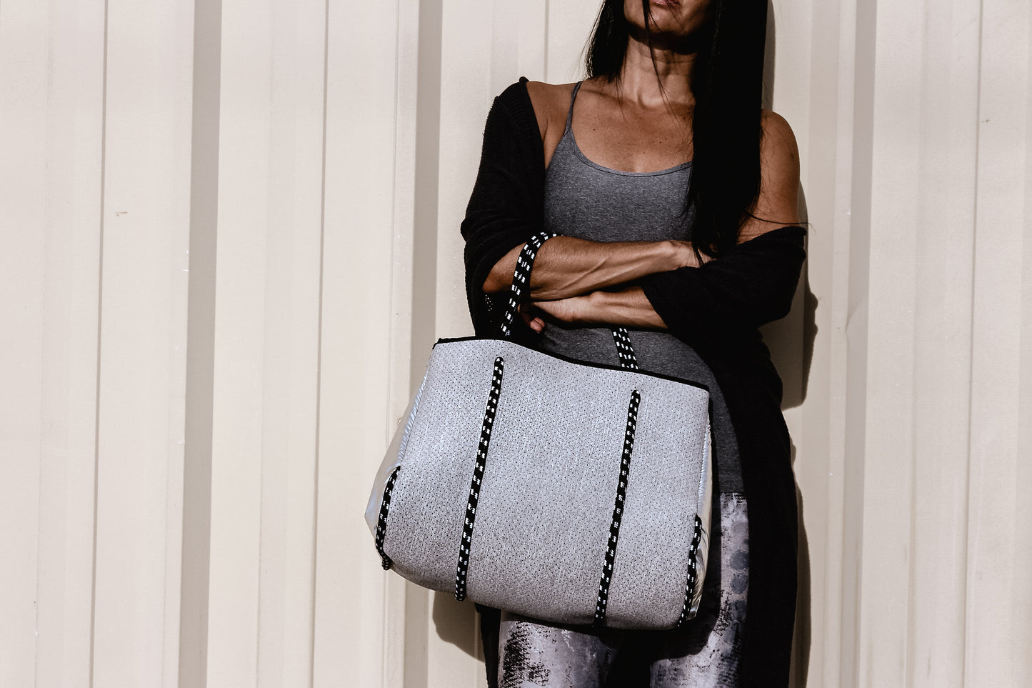 Person holding the Anya & Niki gray neoprene tote bag with shiny silver adjustable sides and cord handles. 